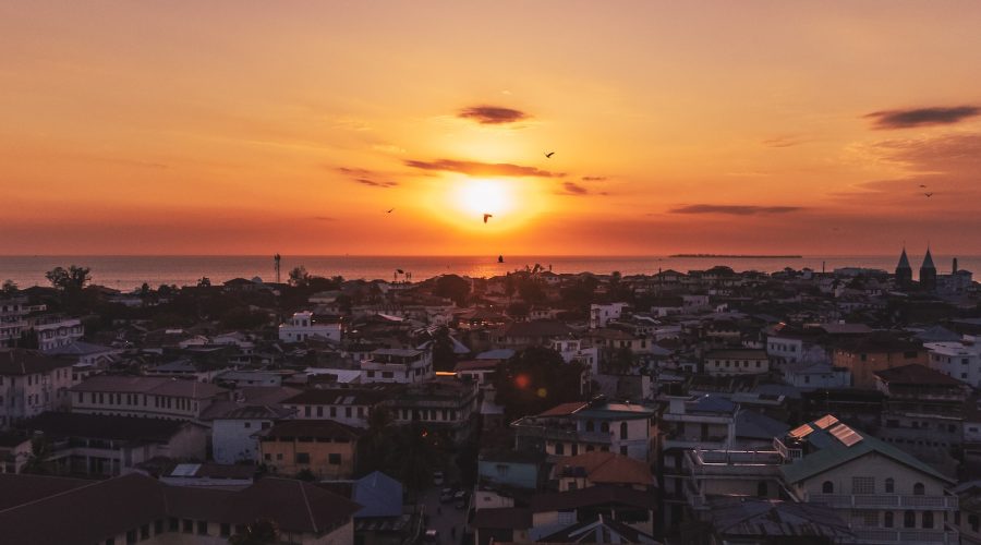 the sun is setting over a city by the ocean