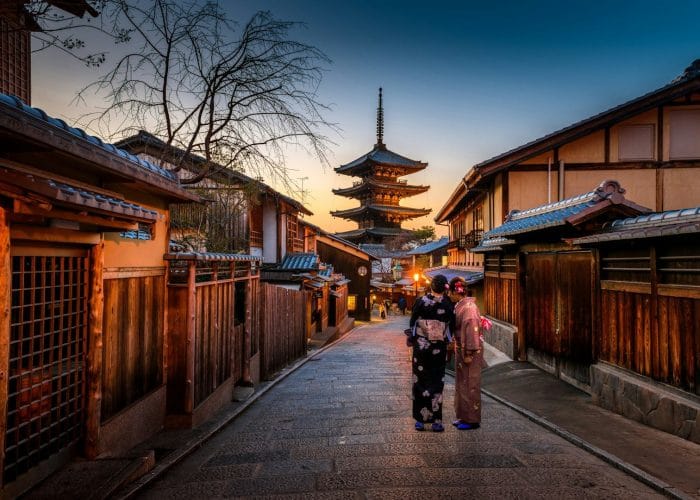 two women in purple and pink kimono standing on street