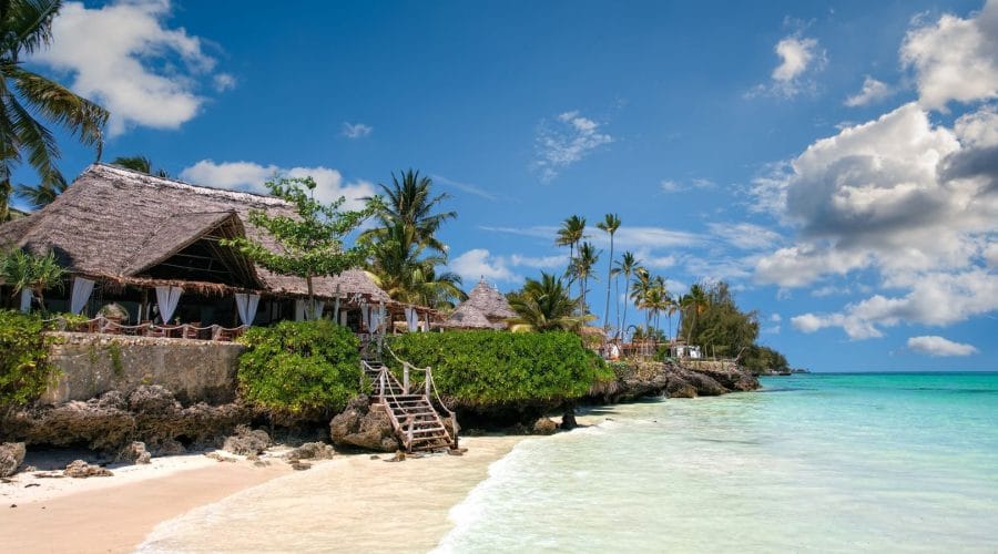 Idyllic beachfront scene in Zanzibar with palm trees, turquoise sea, and a traditional villa.